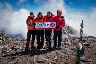 four hikers with red fox banner at summit of mountain